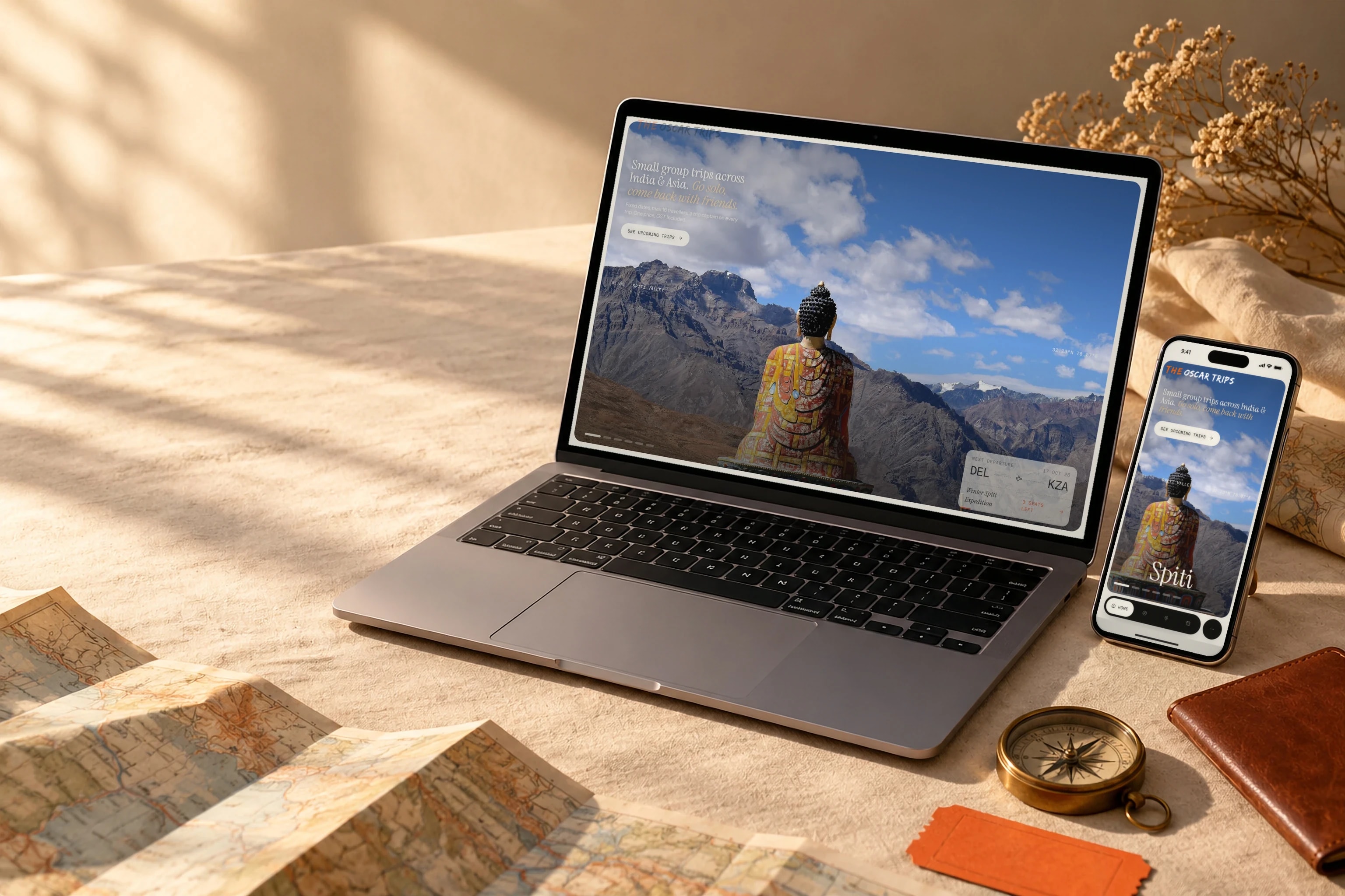 The Oscar Trips site on a laptop and a phone, on a linen table with a map, a passport and a ticket stub.
